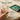 Hand holding a glass with an empty pouch of Hona Fiber + Greens packaging on a kitchen counter.