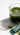 Glass of green juice with a Hona matcha powder packet on a white background