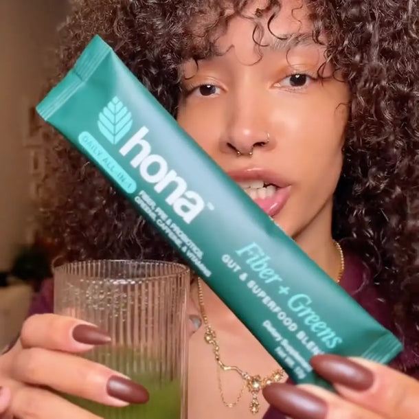 Woman holding a packet of Hona Fiber + Greens explaining the benefits of using the product.